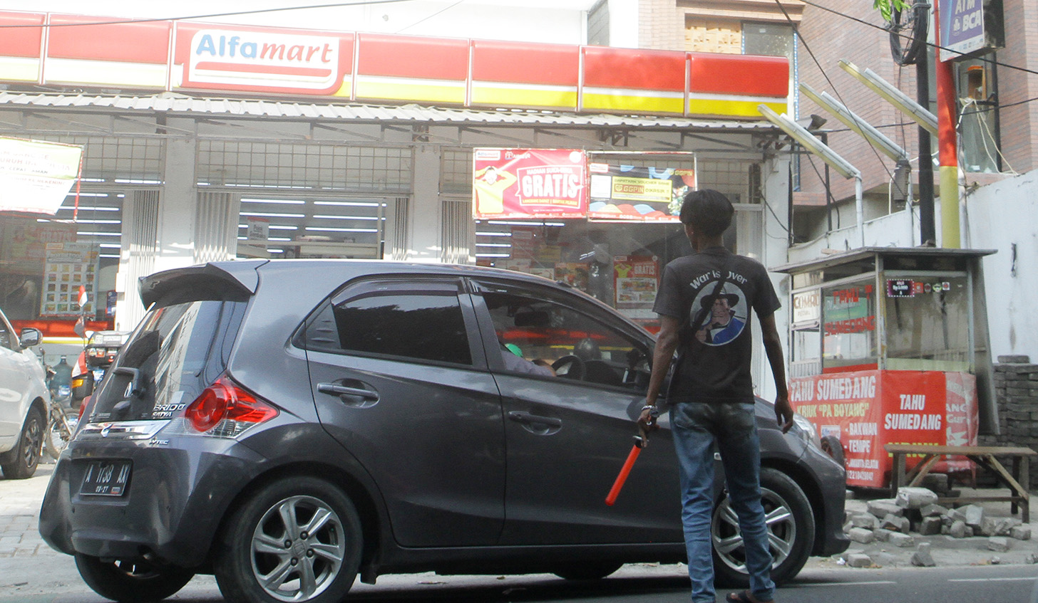 Juru parkir memarkirkan kendaraan di salah satu minimarket di kawasan Jakarta, Senin (13/5/2024). (BeritaNasional.com/Oke Atmaja)