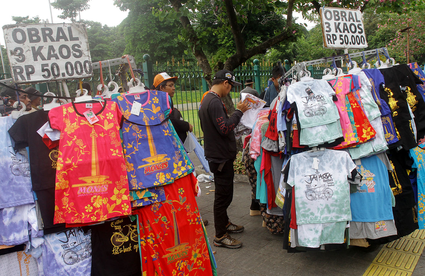 Buruh berbelanja kaos bergambar monas di kawasan Monumen Nasional (Monas), Jakarta, Rabu (1/5/2024). (BeritaNasional.Com/Oke Atmaja)