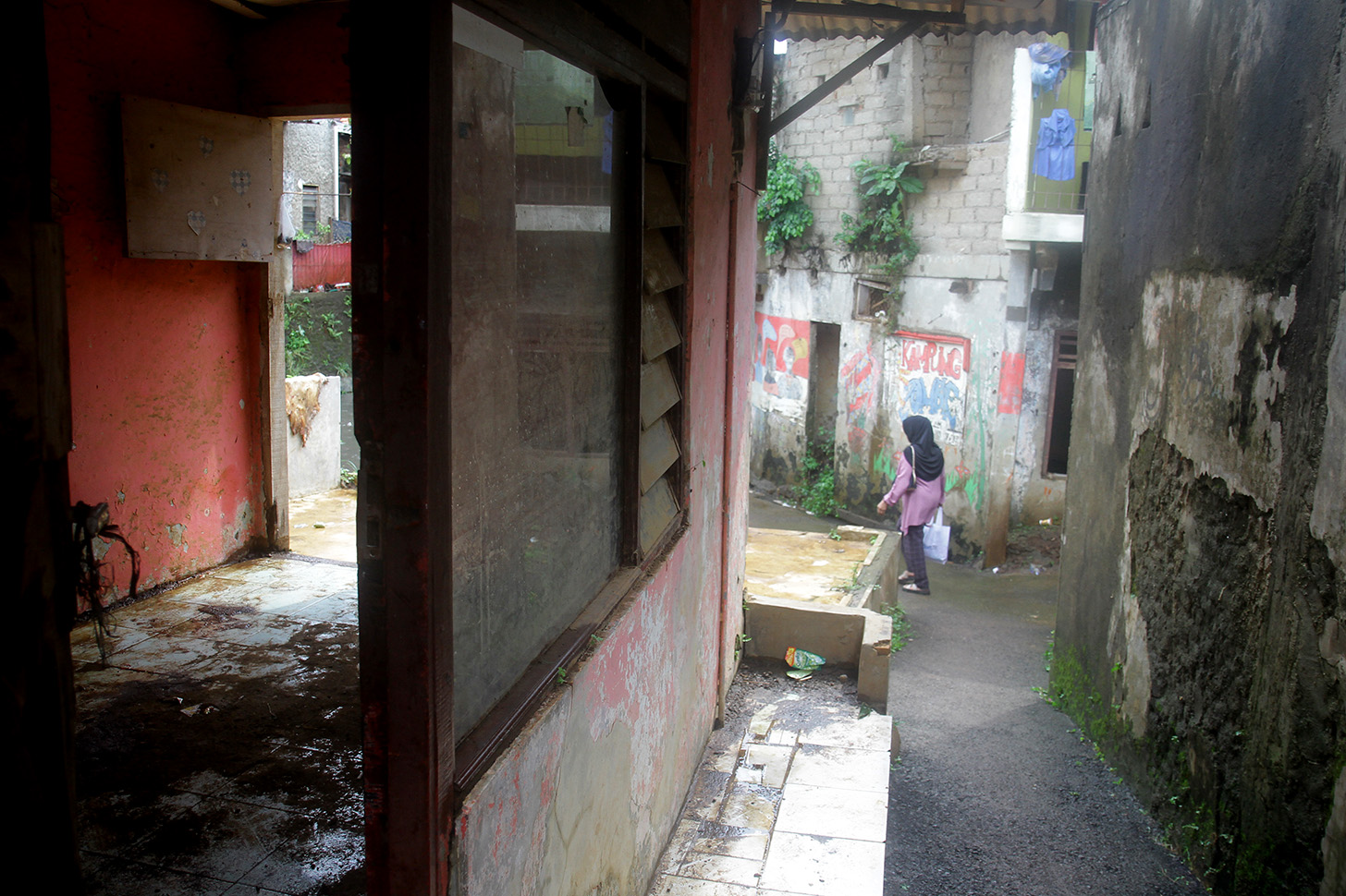Warga berjalan di dekat rumah yang rusak akibat sering terendam banjir di Kampung Zombie Kawasan Cilitan, Jakarta, Selasa (18/6/2024).(BeritaNasional.Com/Oke Atmaja)