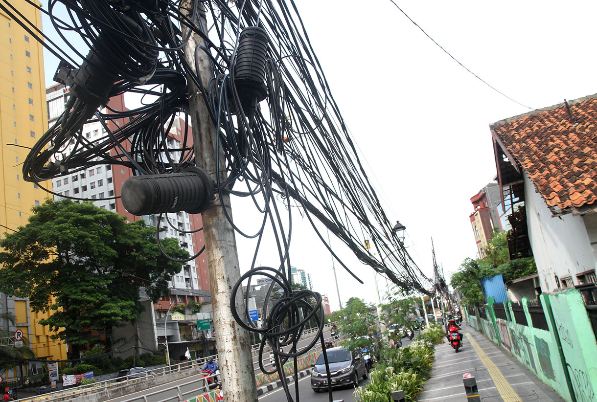 Sejumlah pengendara sepeda motor melintasi jalur pedestrian di bawah kabel yang semrawut di Jalan Matraman Raya, Jakarta, Senin (18/11/2024).  (BeritaNasional.com/Oke Atmaja)