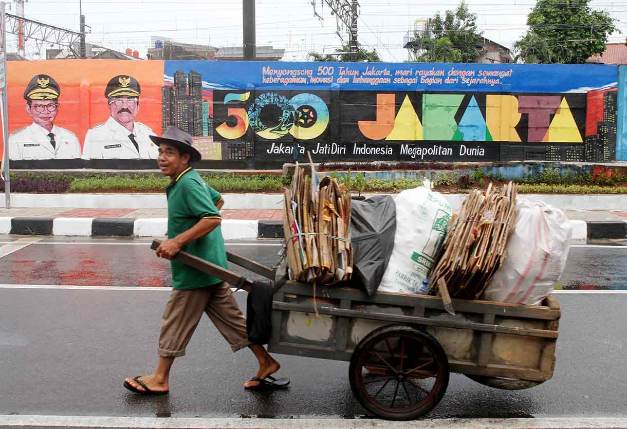 Pedagang melintas di depan mural dengan tema peringatan 500 tahun Jakarta di Jalan Bukit Duri, Jakarta, Sabtu (14/6/2025).(Beritanasional.com/Oke Atmaja)
