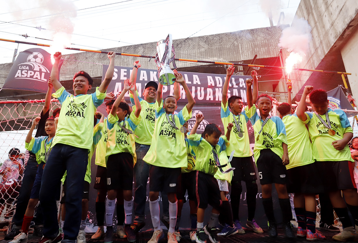 Sejumlah anak yang tergabung dalam tim Blue Lion mengangkat piala usai bertanding pada Liga Aspal di kawasan Menteng, Jakarta, Sabtu (18/7/2026). (Beritanasional.com/Oke Atmaja)