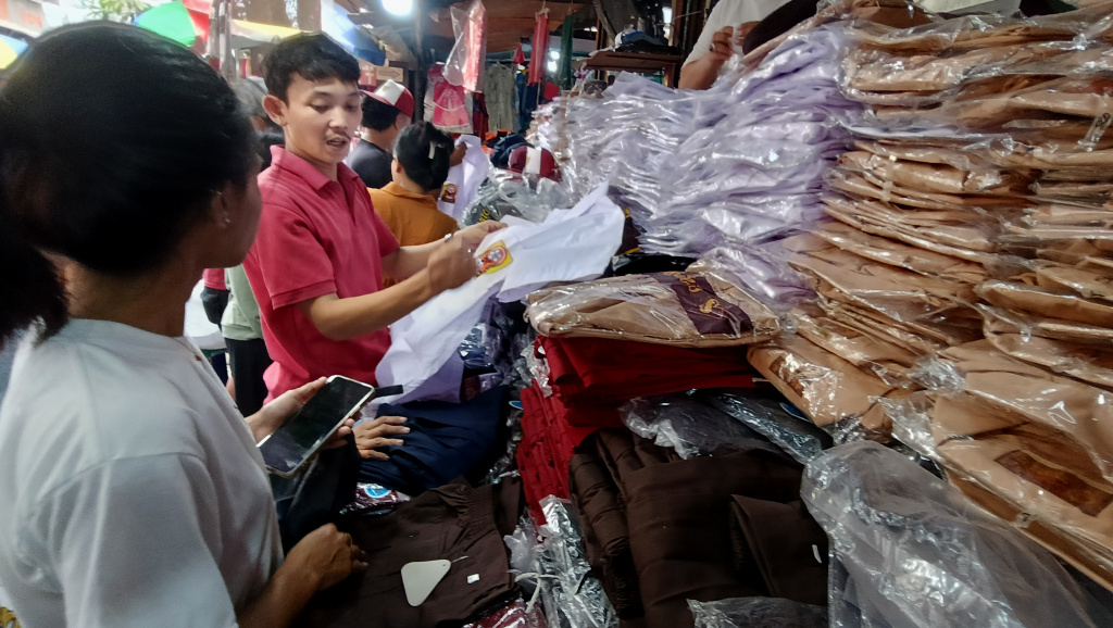 Pedagang melayani calon pembeli seragam sekolah di Pasar Jatinegara, Jakarta, Minggu (12/7/2026). (Beritanasional.com/Oke Atmaja)