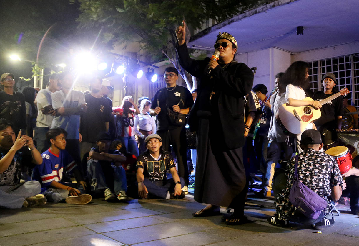 Massa aksi dari sejumlah seniman, konten creator dan masyarakat membawa poster dukungan produk UMKM konveksi pada Aksi Seni di Kota Tua, Jakarta, Minggu, Malam (16/11/2025).(Beritanasional.com/Oke Atmaja)