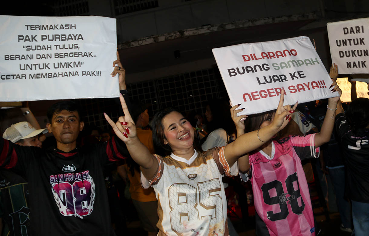 Massa aksi dari sejumlah seniman, konten creator dan masyarakat membawa poster dukungan produk UMKM konveksi pada Aksi Seni di Kota Tua, Jakarta, Minggu, Malam (16/11/2025).(Beritanasional.com/Oke Atmaja)