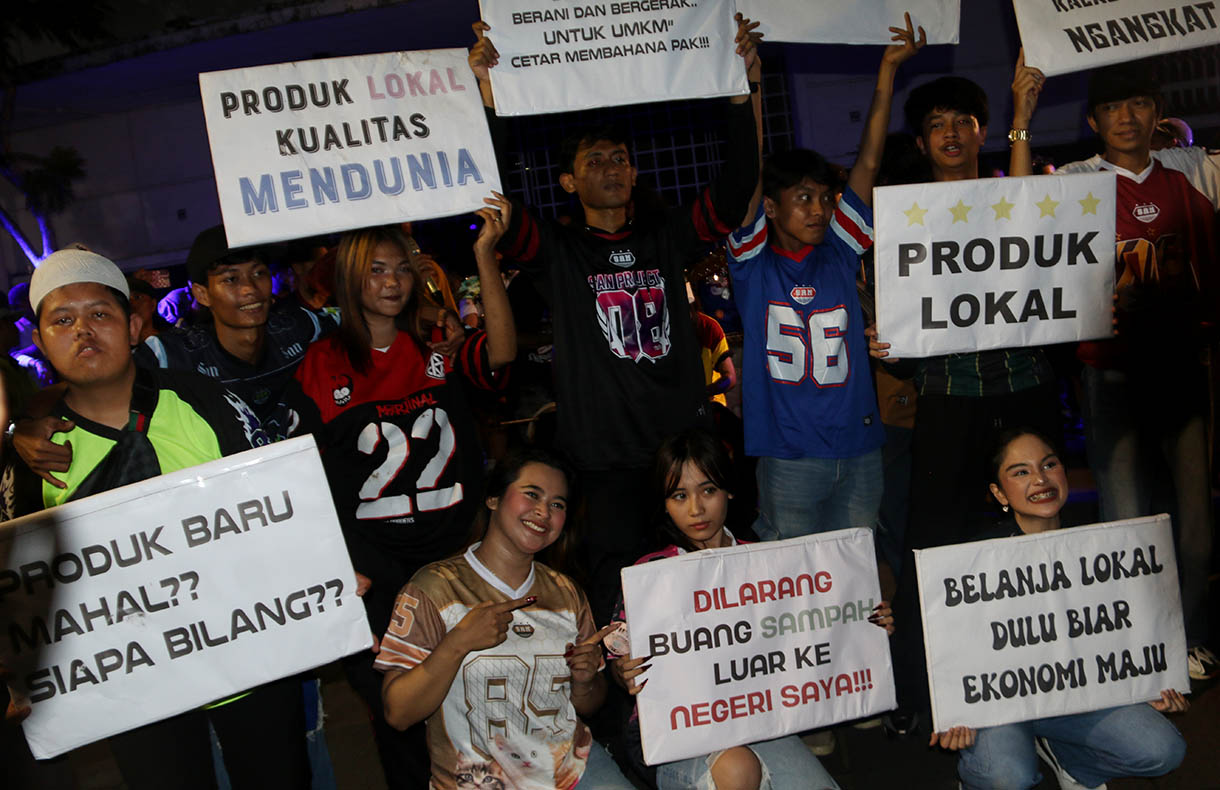Massa aksi dari sejumlah seniman, konten creator dan masyarakat membawa poster dukungan produk UMKM konveksi pada Aksi Seni di Kota Tua, Jakarta, Minggu, Malam (16/11/2025).(Beritanasional.com/Oke Atmaja)