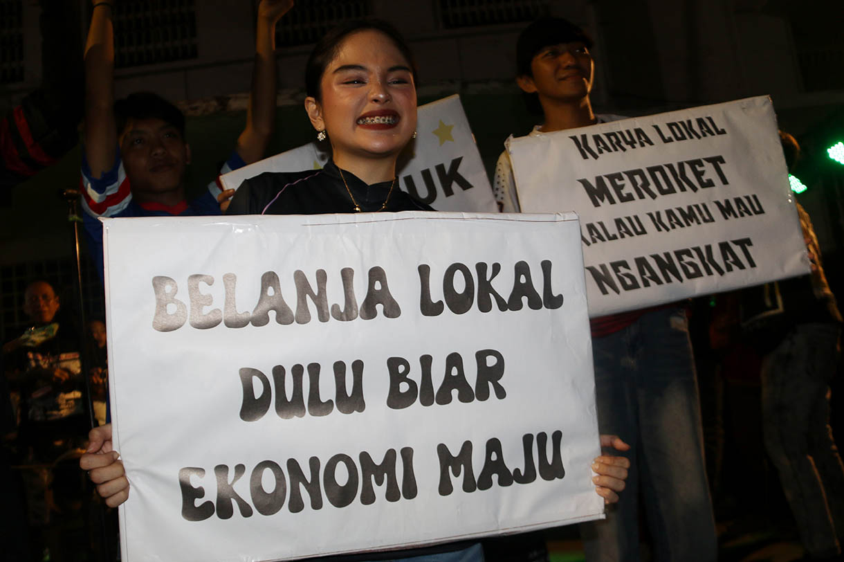 Massa aksi dari sejumlah seniman, konten creator dan masyarakat membawa poster dukungan produk UMKM konveksi pada Aksi Seni di Kota Tua, Jakarta, Minggu, Malam (16/11/2025).(Beritanasional.com/Oke Atmaja)