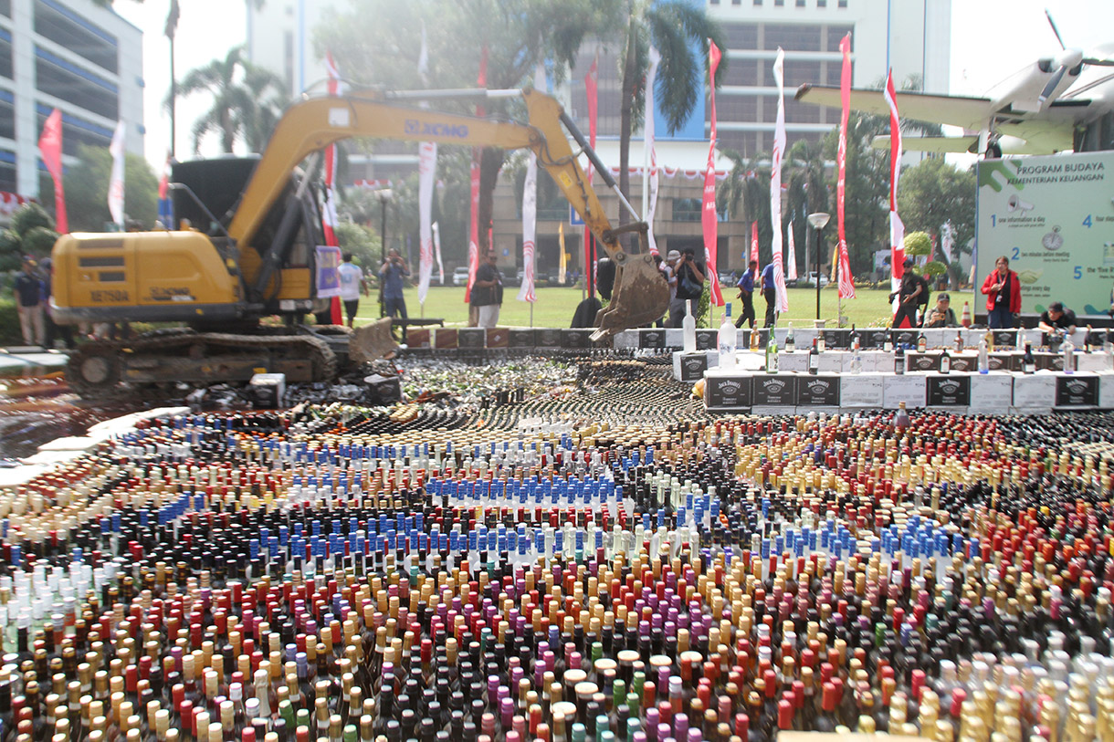 Petugas menggunakan alat berat eskavator saat memusnahkan minuman keras ilegal hasil penindakan di Kantor Pusat Bea Cukai, Jakarta Timur,Rabu (31/7/2024). (BeritaNasional.com/Oke Atmaja)