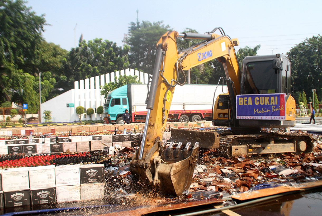 Petugas menggunakan alat berat eskavator saat memusnahkan minuman keras ilegal hasil penindakan di Kantor Pusat Bea Cukai, Jakarta Timur,Rabu (31/7/2024). (BeritaNasional.com/Oke Atmaja)