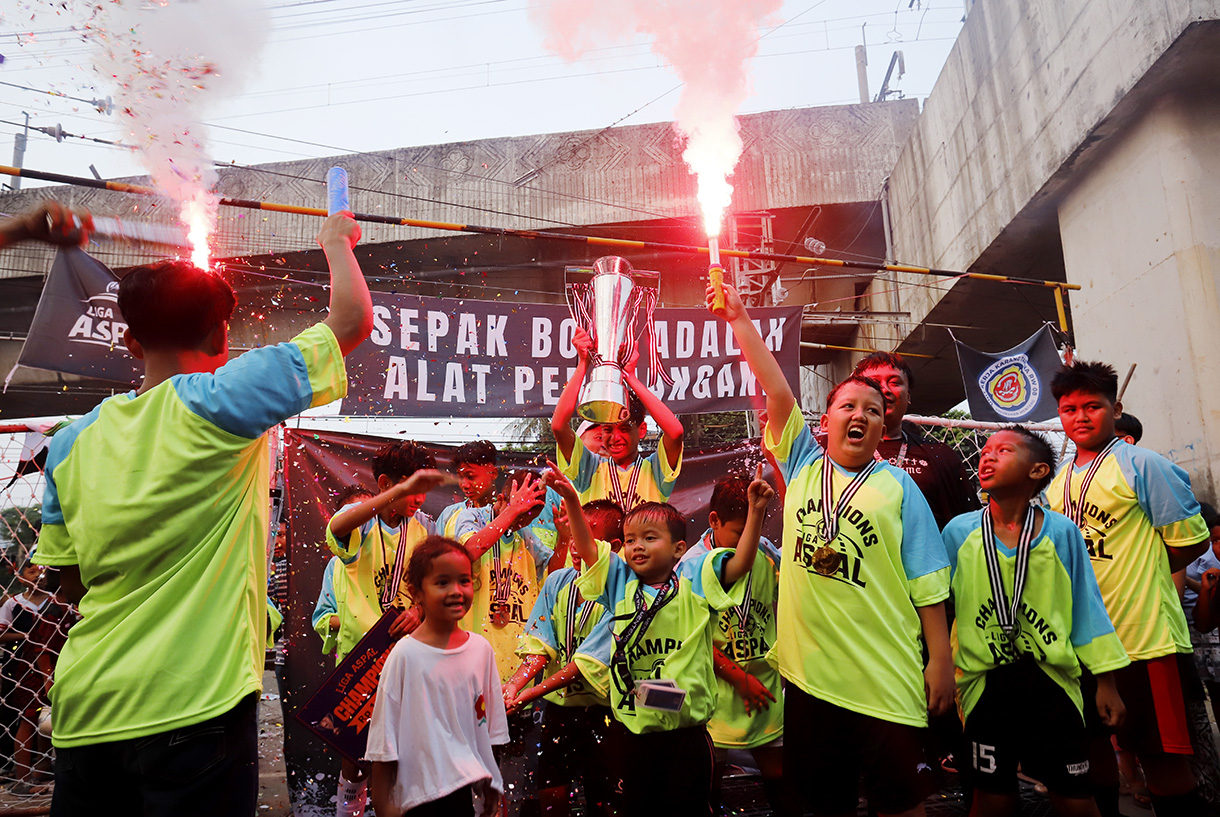 Sejumlah anak yang tergabung dalam tim Blue Lion mengangkat piala usai bertanding pada Liga Aspal di kawasan Menteng, Jakarta, Sabtu (18/7/2026). (Beritanasional.com/Oke Atmaja)