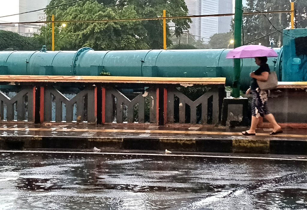 Warga memakai payung melintas di jembatan Stasiun Karet, Jakarta, Sabtu (4/4/2026). (Beritanasional.com/Oke Atmaja)