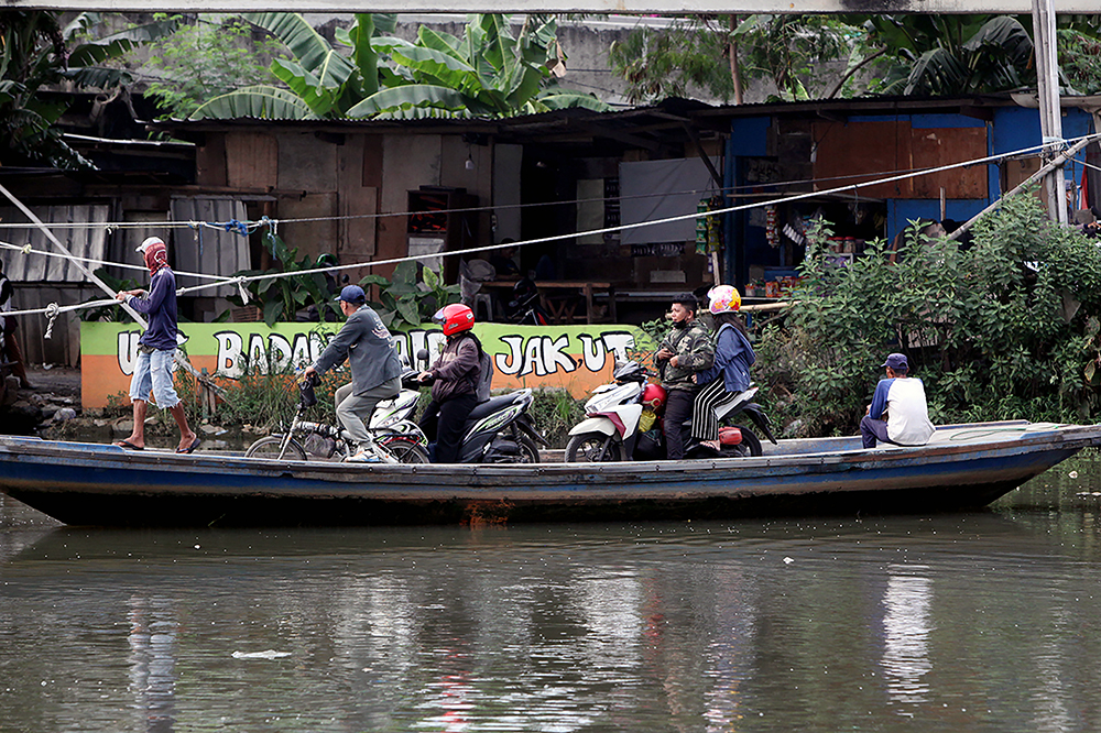 Warga berkendaraan motor saat menyebrang menggunakan perahu eret di Jakarta. (BeritaNasional/Elvis Sendouw)