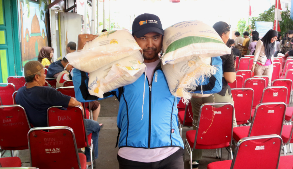 Warga memikul beras usai mengambil bantuan pangan gratis. (Berita nasional.com/Oke Atmaja)