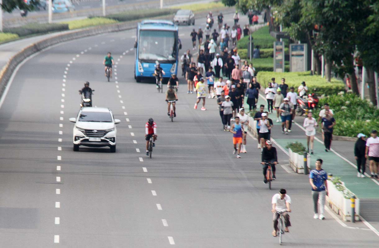 Pengendara motor melintas berdampingan dengan warga yang sedang berolahraga di kawasan Bundaran HI, Jakarta, Minggu (31/5/2026).(Beritanasional.com/Oke Atmaja)