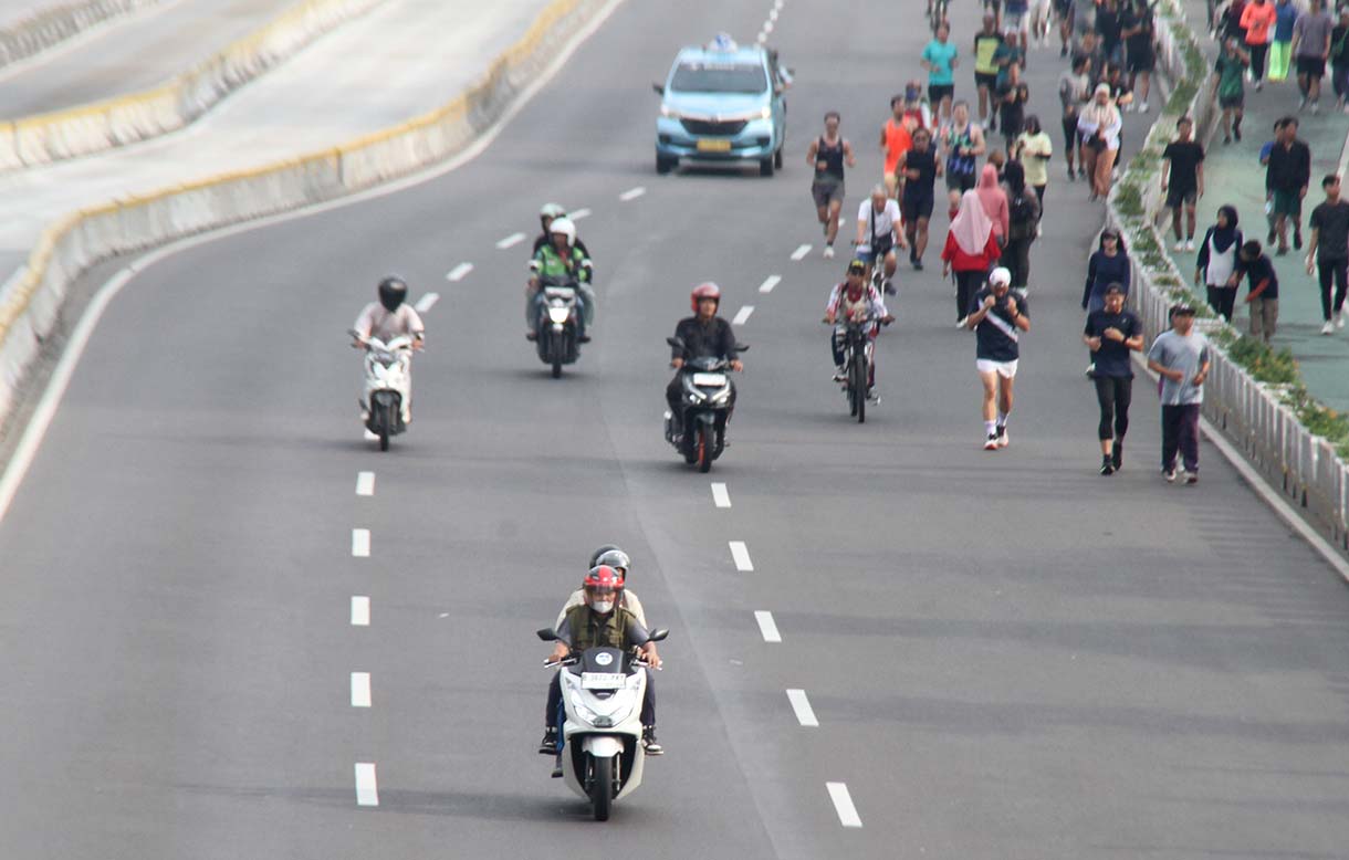 Pengendara motor melintas berdampingan dengan warga yang sedang berolahraga di kawasan Bundaran HI, Jakarta, Minggu (31/5/2026).(Beritanasional.com/Oke Atmaja)