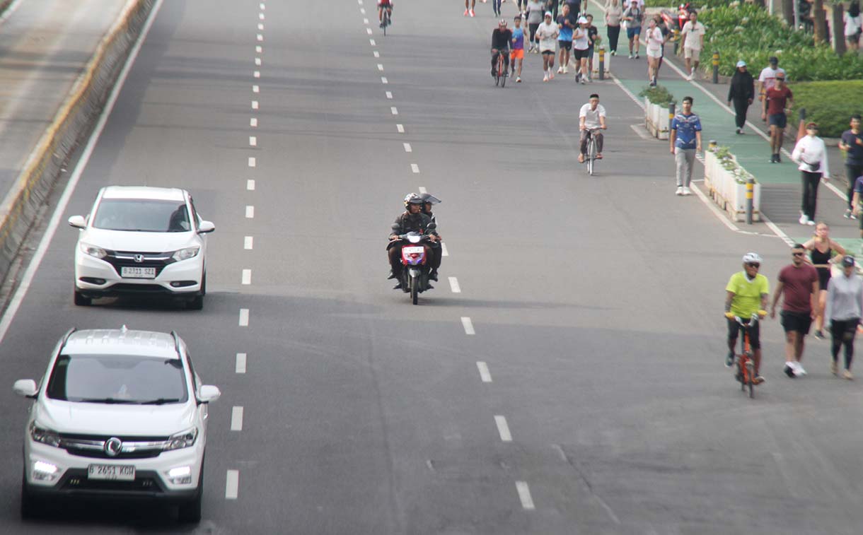 Pengendara motor melintas berdampingan dengan warga yang sedang berolahraga di kawasan Bundaran HI, Jakarta, Minggu (31/5/2026).(Beritanasional.com/Oke Atmaja)