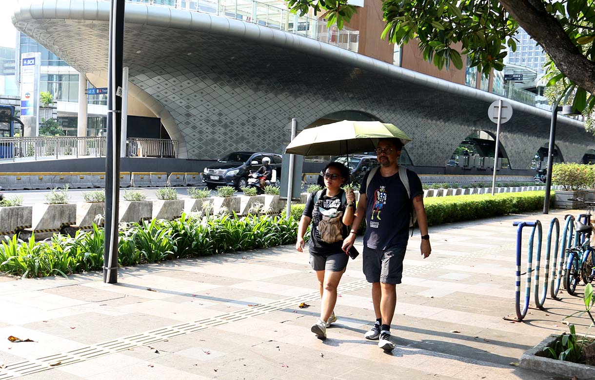Warga mengenakan penutup kepala saat cuaca terik di kawasan Bundaran HI, Jakarta, Rabu (15/10/2025). (Beritanasional.com/Oke Atmaja)