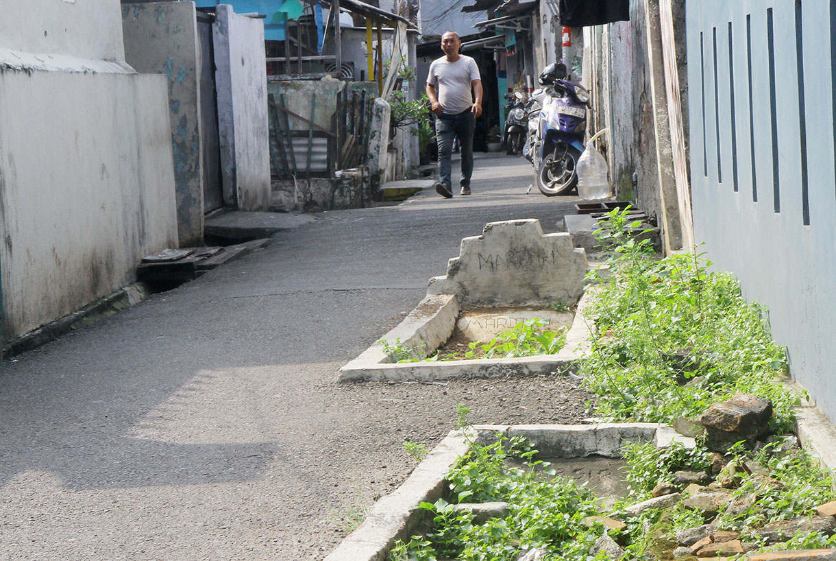 Warga melintas disamping kuburan di gang RT 03 RW 04 Kelurahan Pisangan Timur,Jakarta, Sabtu (13/7/2024) .(BeritaNasional.com/Oke Atmaja)