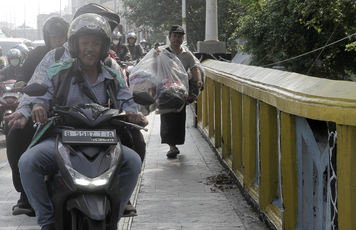 Warga berjalan di dekat pengendara motor yang melintasi trotoar di Jalan Matraman Raya, Jakarta, Selasa (26/4/2024).(Indonesiaglobe/Oke Atmaja)