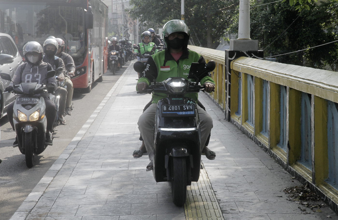 Warga berjalan di dekat pengendara motor yang melintasi trotoar di Jalan Matraman Raya, Jakarta, Selasa (26/4/2024).(Indonesiaglobe/Oke Atmaja)