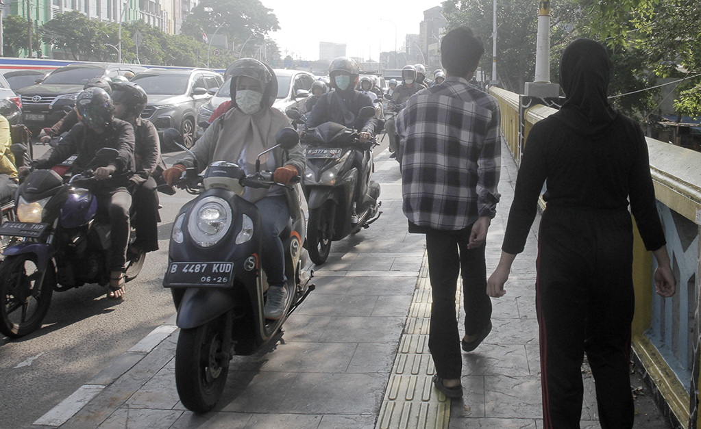 Warga berjalan di dekat pengendara motor yang melintasi trotoar di Jalan Matraman Raya, Jakarta, Selasa (26/4/2024).(Indonesiaglobe/Oke Atmaja)