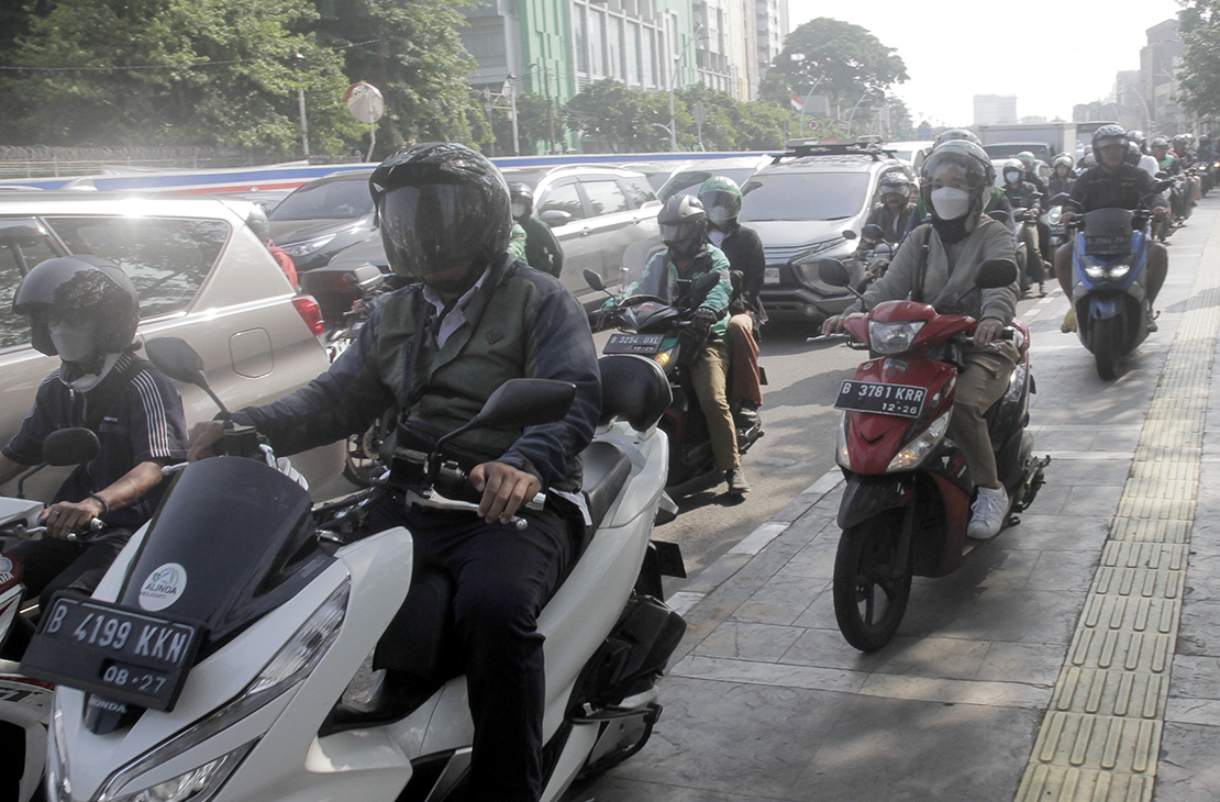 Warga berjalan di dekat pengendara motor yang melintasi trotoar di Jalan Matraman Raya, Jakarta, Selasa (26/4/2024).(Indonesiaglobe/Oke Atmaja)