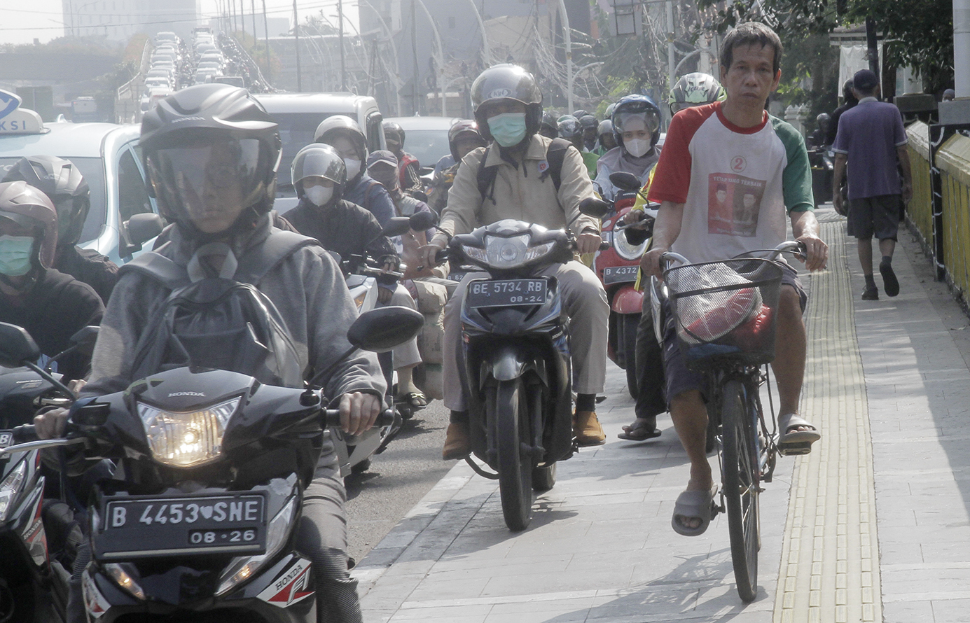 Warga berjalan di dekat pengendara motor yang melintasi trotoar di Jalan Matraman Raya, Jakarta, Selasa (26/4/2024).(Indonesiaglobe/Oke Atmaja)