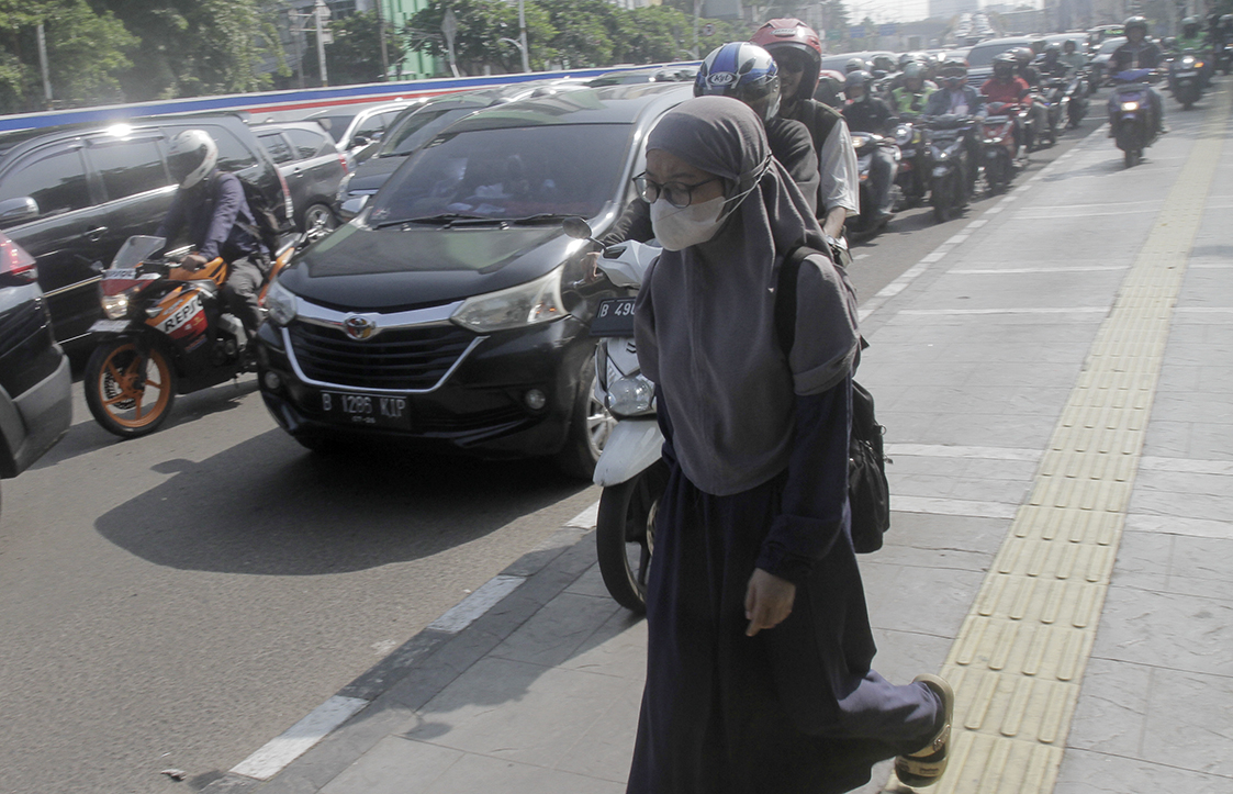 Warga berjalan di dekat pengendara motor yang melintasi trotoar di Jalan Matraman Raya, Jakarta, Selasa (26/4/2024).(Indonesiaglobe/Oke Atmaja)