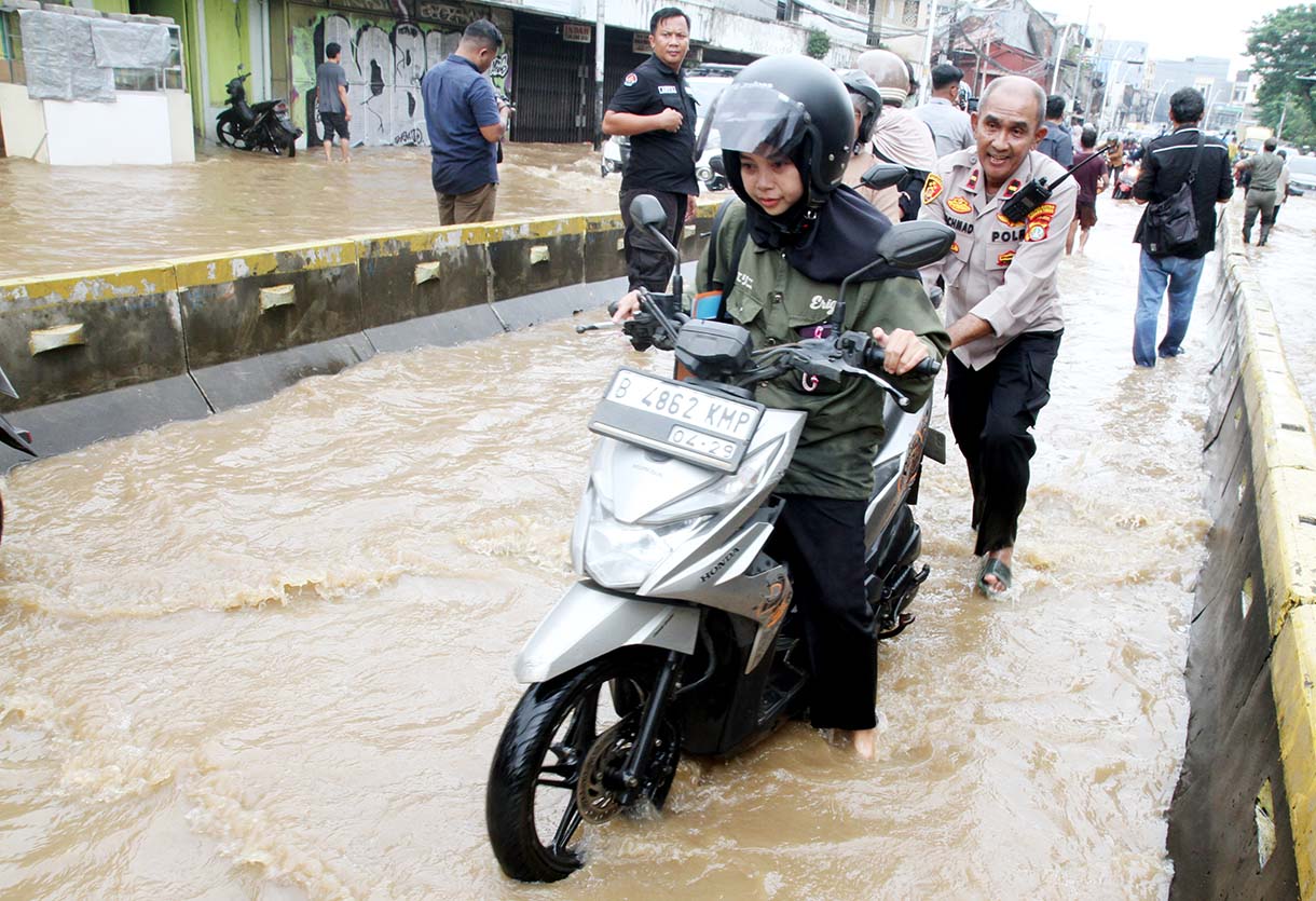 Warga melintasi banjir yang merendam rumah makan di jalan Jatinegara Barat, Jakarta, Selasa (4/3/2025).  (Beritanasional.com/Oke Atmaja)