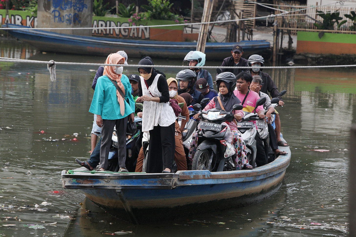 Sejumlah pengendara sepeda motor menggunakan perahu eretan menyeberangi Sungai Kali Angke di Kecamatan Penjaringan, Jakarta, Kamis (30/5/2024). (BeritaNasional.Com/Oke Atmaja)