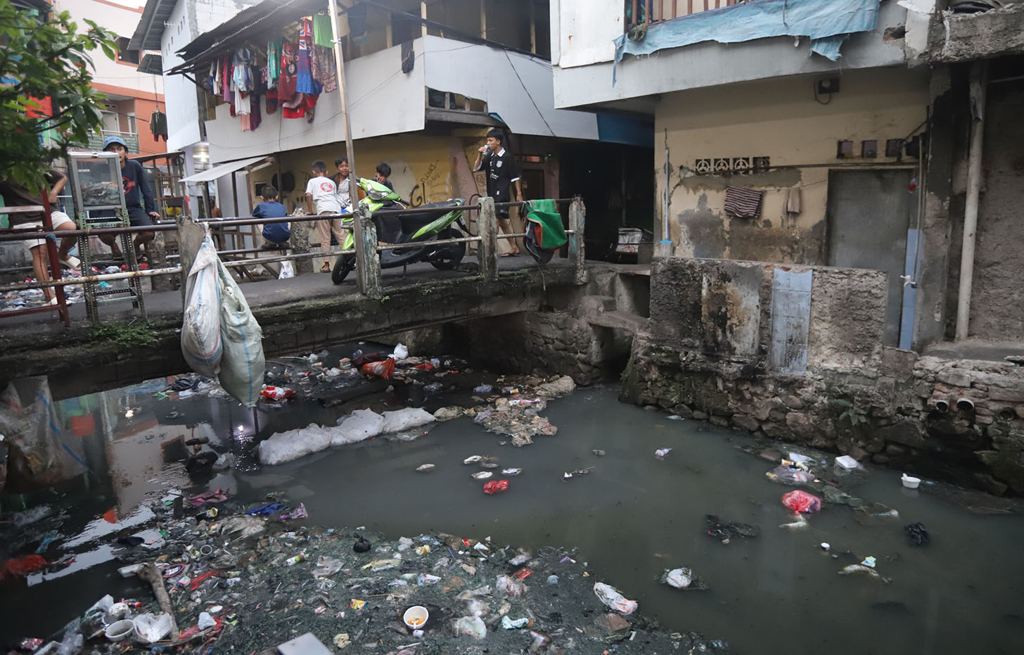 Warga melintas di pinggir aliran Sungai Ciliwung Kecil di kawasan Kebon Kacang, Tanah Abang, Jakarta, Selasa (25/6/2024). (BeritaNasional.Com/Oke Atmaja)