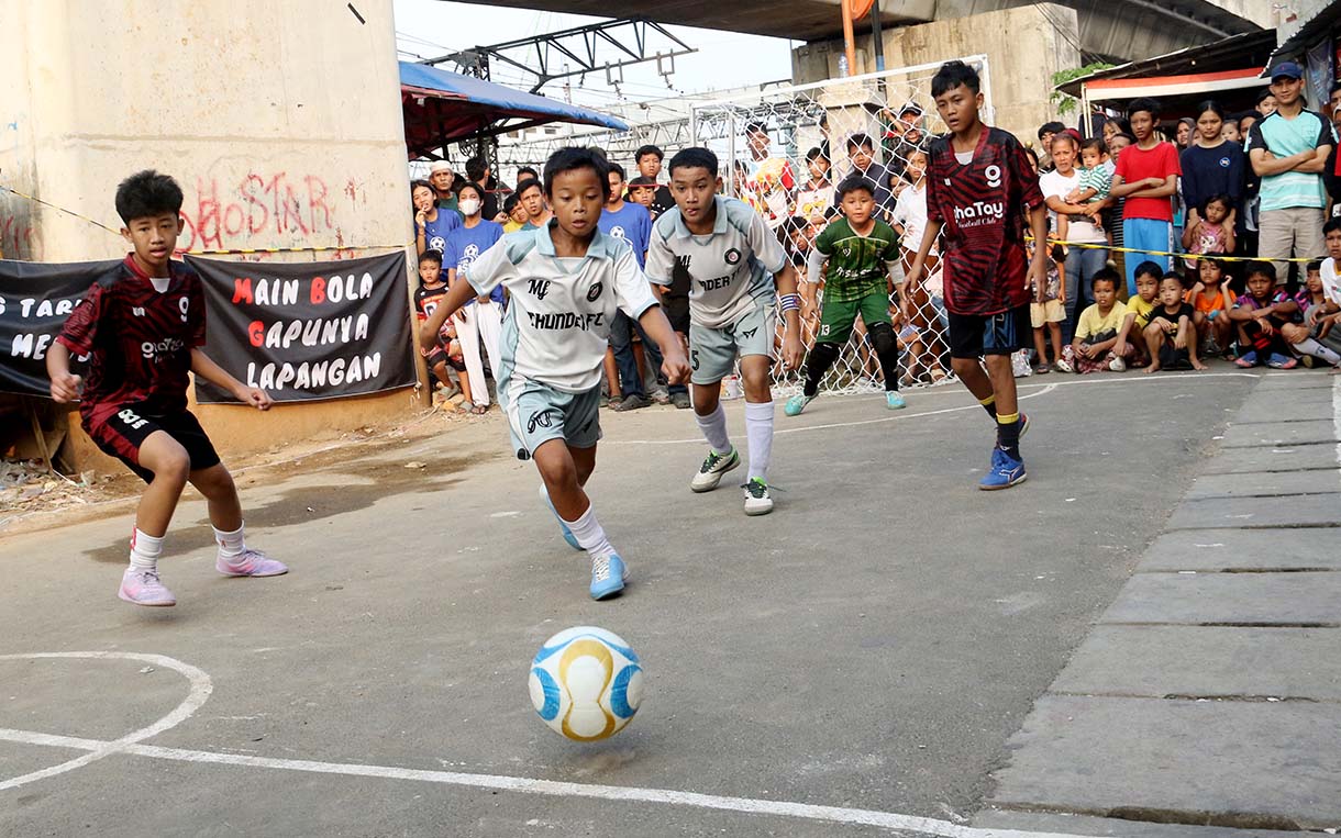 Anak-anak mengikuti pertandingan Turnamen Sepak Bola "Liga Aspal" U-13 di lapangan sederhana kawasan permukiman padat pinggir rel RT 09/RW 08, Menteng Jaya, Jakarta, Sabtu (20/6/2026). (Beritanasional.com/Oke Atmaja)