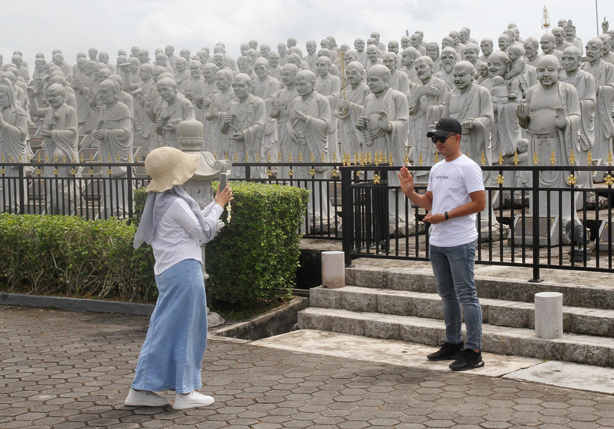 Wisatawan berfoto di objek 500 Patung Budha dengan seribu ekpresi wajah murid Budha yang telah mencapai kesucian spritual tertinggi atau sering disebut Arahat, yang merupakan koleksi dari Vihara Ksitigarbha Bodhisattva di Tanjung pinang, Kepri, Kamis(5/12/2024).  (BeritaNasional.com/Oke Atmaja)