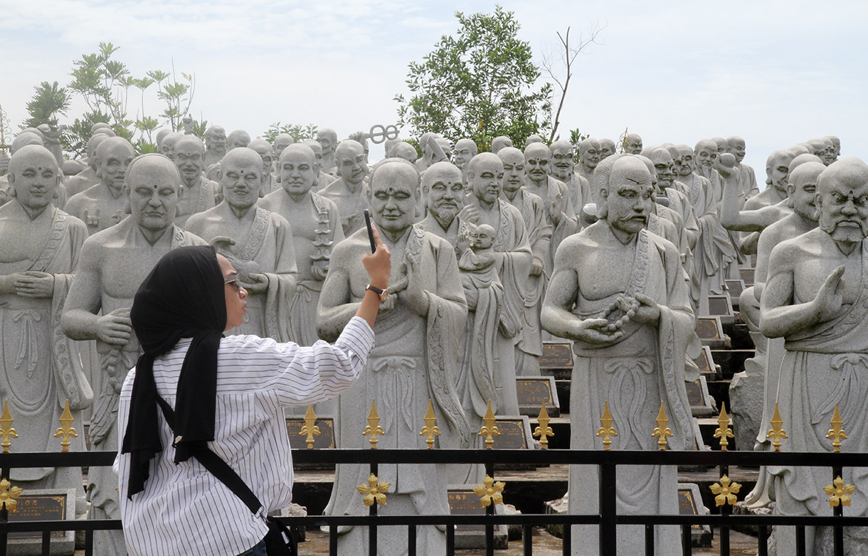 Wisatawan berfoto di objek 500 Patung Budha dengan seribu ekpresi wajah murid Budha yang telah mencapai kesucian spritual tertinggi atau sering disebut Arahat, yang merupakan koleksi dari Vihara Ksitigarbha Bodhisattva di Tanjung pinang, Kepri, Kamis(5/12/2024).  (BeritaNasional.com/Oke Atmaja)