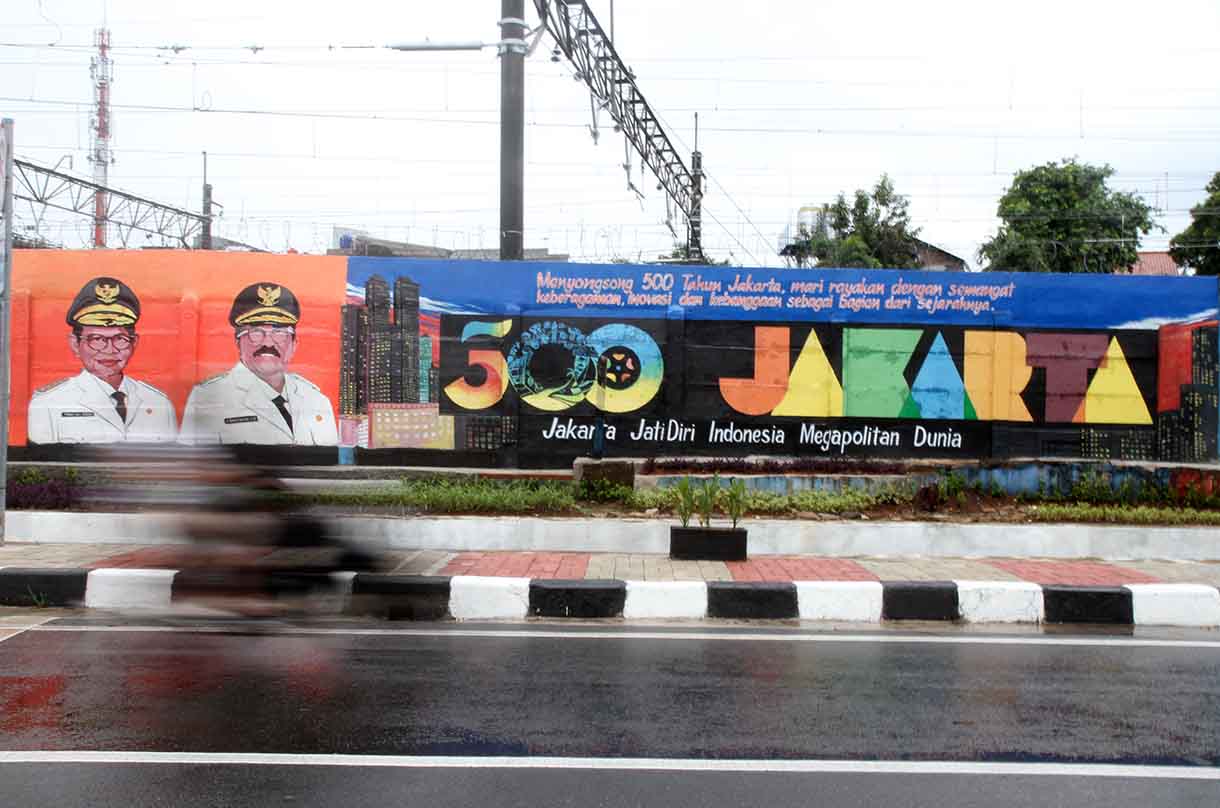 Pedagang melintas di depan mural dengan tema peringatan 500 tahun Jakarta di Jalan Bukit Duri, Jakarta, Sabtu (14/6/2025).(Beritanasional.com/Oke Atmaja)