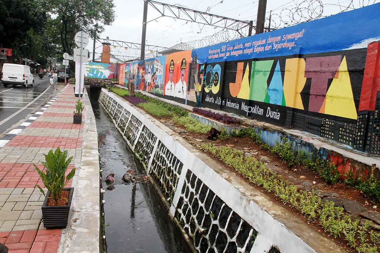 Pedagang melintas di depan mural dengan tema peringatan 500 tahun Jakarta di Jalan Bukit Duri, Jakarta, Sabtu (14/6/2025).(Beritanasional.com/Oke Atmaja)