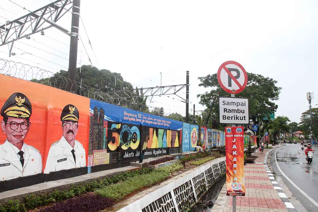 Pedagang melintas di depan mural dengan tema peringatan 500 tahun Jakarta di Jalan Bukit Duri, Jakarta, Sabtu (14/6/2025).(Beritanasional.com/Oke Atmaja)
