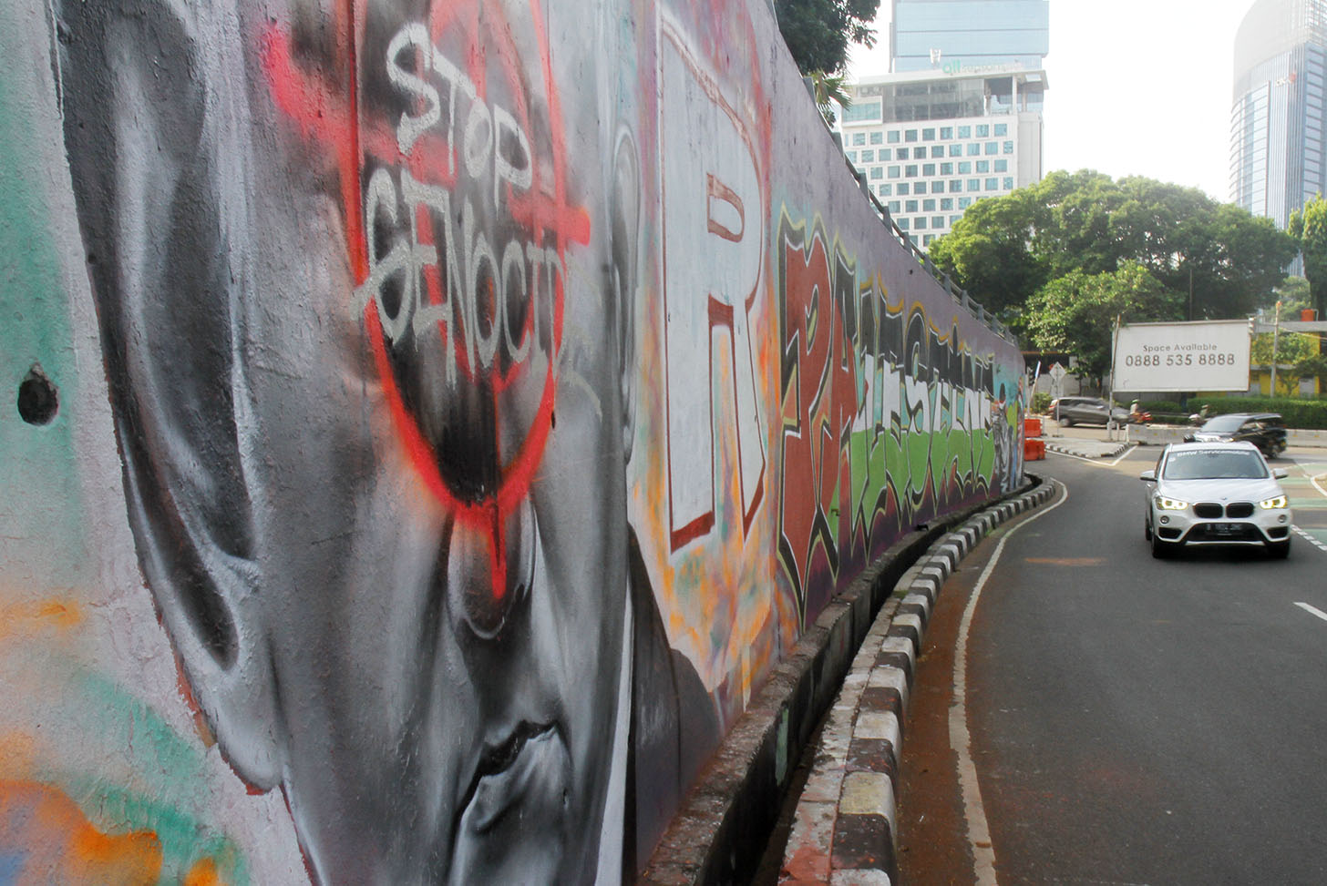 Pengendara sepeda motor melintasi mural dengan gambar wajah PM Israel, Benjamin Netanyahu dengan tulisan Stop Genocide di Kawasan Sudirman, Jakarta, Jumat(21/6/2024).(BeritaNasional.Com/Oke Atmaja)