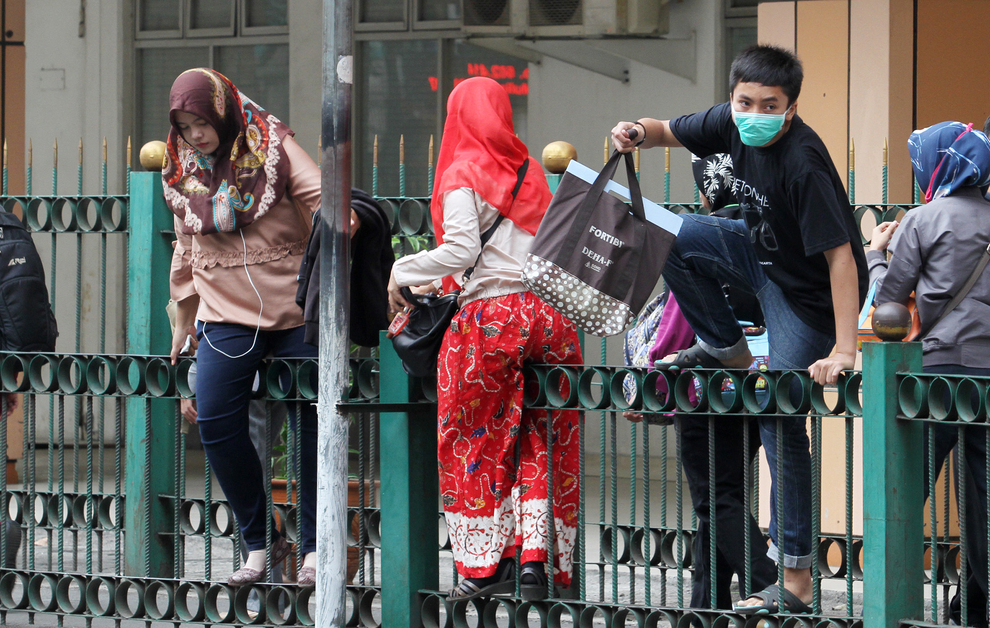 Penumpang KRL melompati pagar pembatas di depan Stasiun Cikini, Jalan Cikini Raya, Jakarta Pusat, Rabu (20/3/2024).  (IndonesiaGlobe/Oke Atmaja)