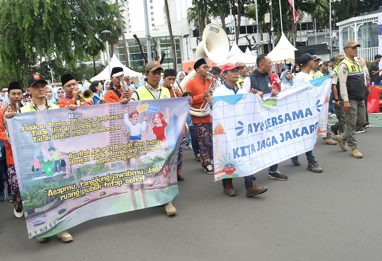 Sejumlah peserta membawa spanduk berisi imbauan untuk menjaga kebersihan dan ketertiban saat mengikuti pawai pada Hari Bebas Kendaraan Bermotor (HBKB) di kawasan Bundaran HI, Jakarta Pusat, Minggu (16/11/2025).(Beritanasional.com/Oke Atmaja)