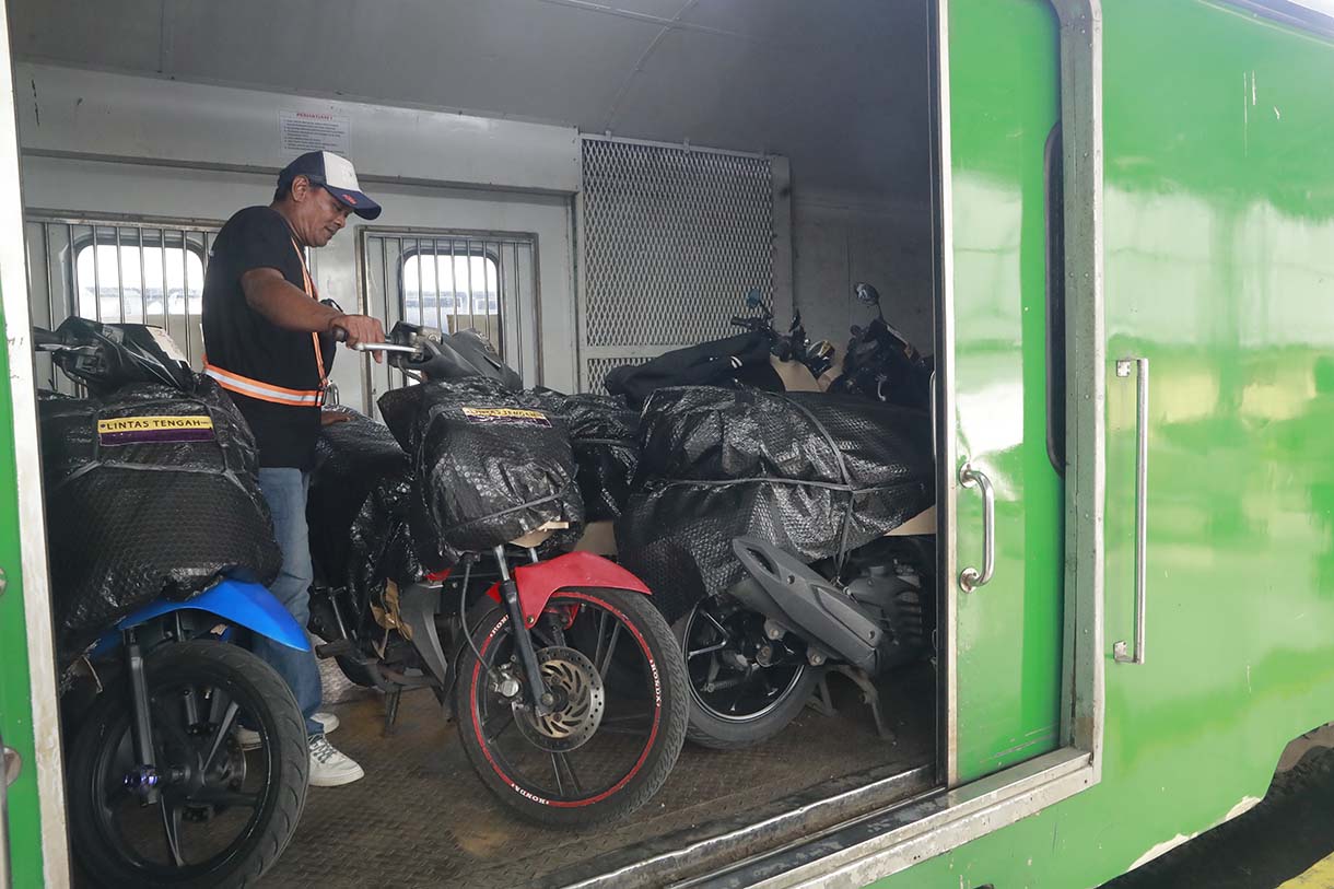 Petugas merapikan motor penumpang peserta layanan Angkutan Motor Gratis dengan Kereta Api (Motis) di dalam gerbong kereta api di Stasiun Pasar Senen, Jakarta, Selasa (23/12/2025).  (Beritanasional.com/Oke Atmaja)