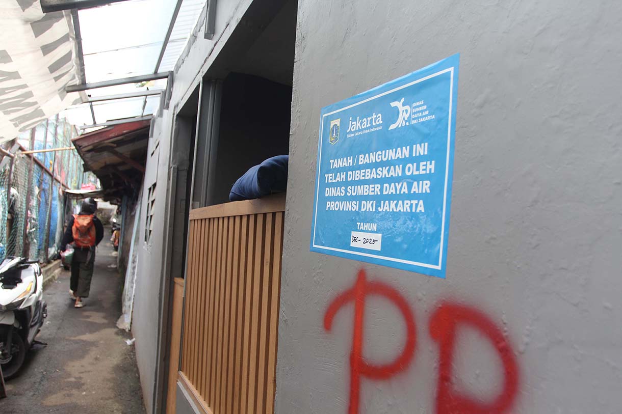 Warga melintas didekat bangunan rumah yang tertempel stiker tanda pembebasan lahan di Cawang, Jakarta, Senin (3/2/2026).(Beritanasional.com/Oke Atmaja)