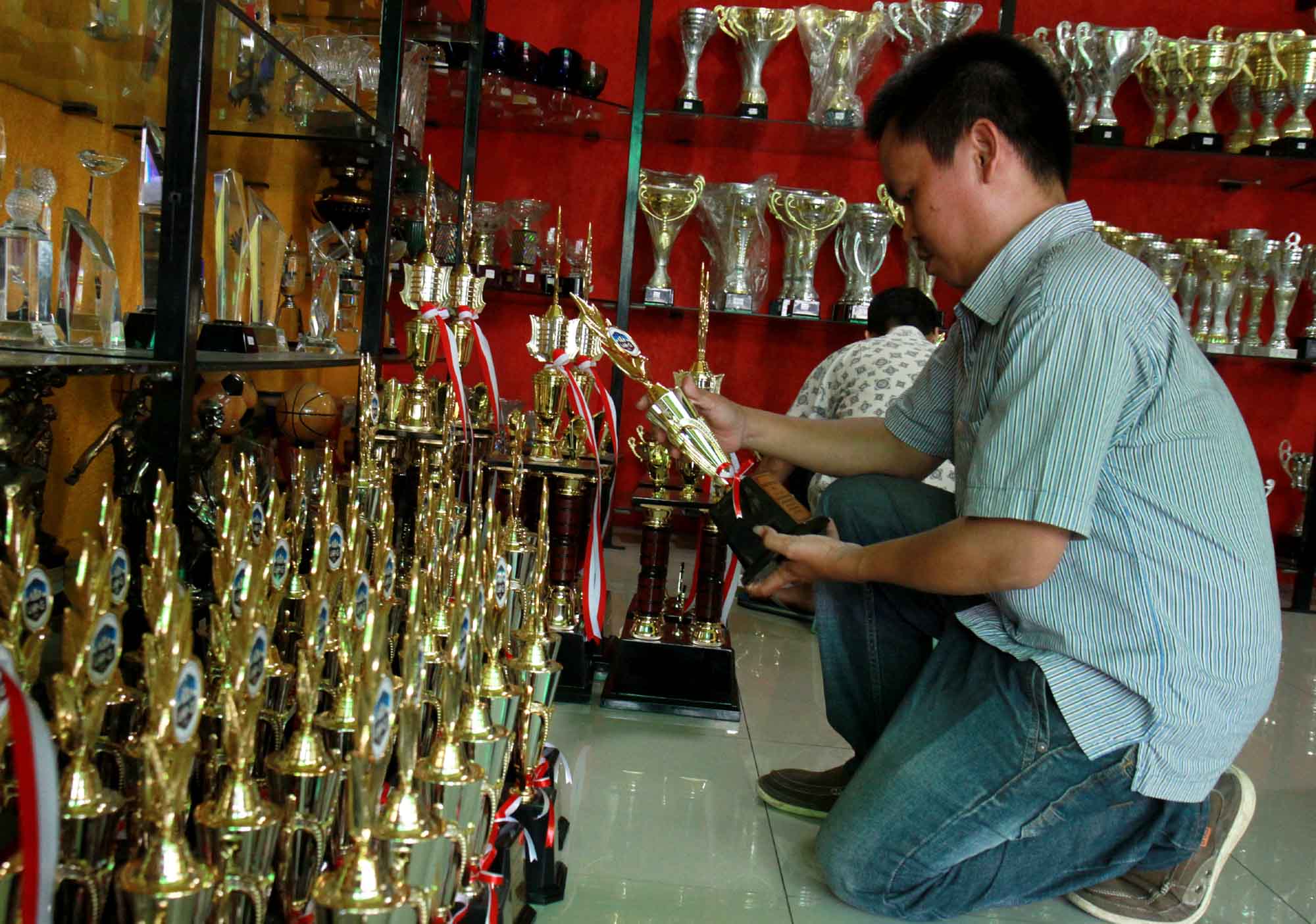 Pengrajin menyelesaikan proses pembuatan piala di tokonya di kawasan Senen, Jakarta, Selasa (6/8/2024) (BeritaNasional.com/Oke Atmaja)