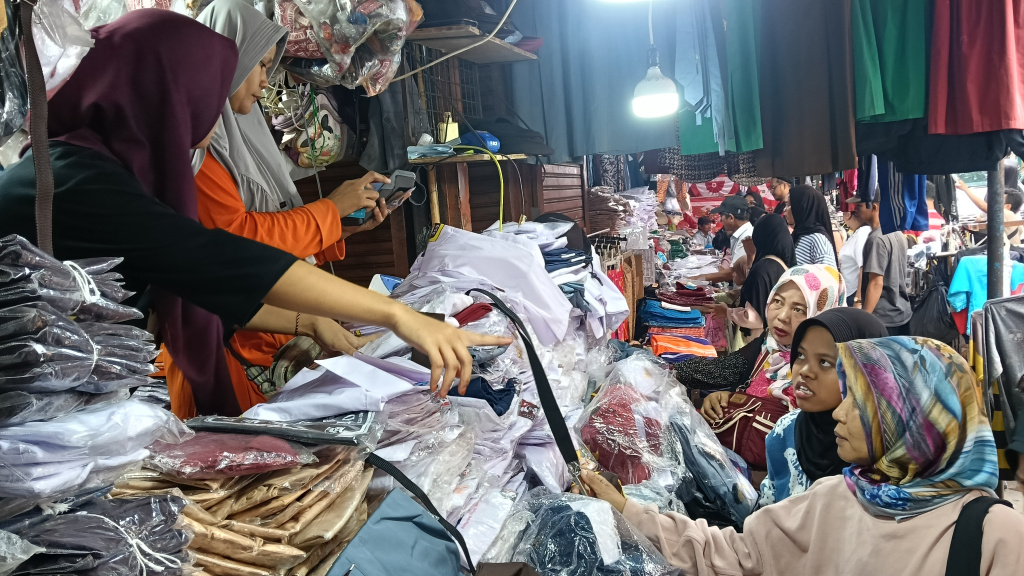 Pedagang melayani calon pembeli seragam sekolah di Pasar Jatinegara, Jakarta, Minggu (12/7/2026). (Beritanasional.com/Oke Atmaja)