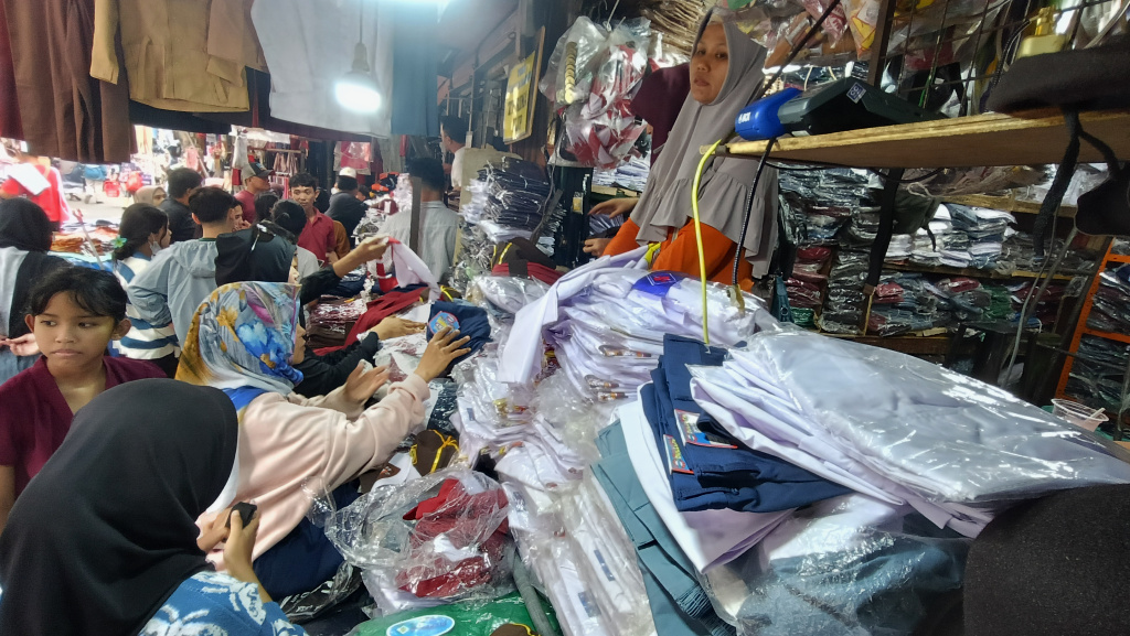Pedagang melayani calon pembeli seragam sekolah di Pasar Jatinegara, Jakarta, Minggu (12/7/2026). (Beritanasional.com/Oke Atmaja)