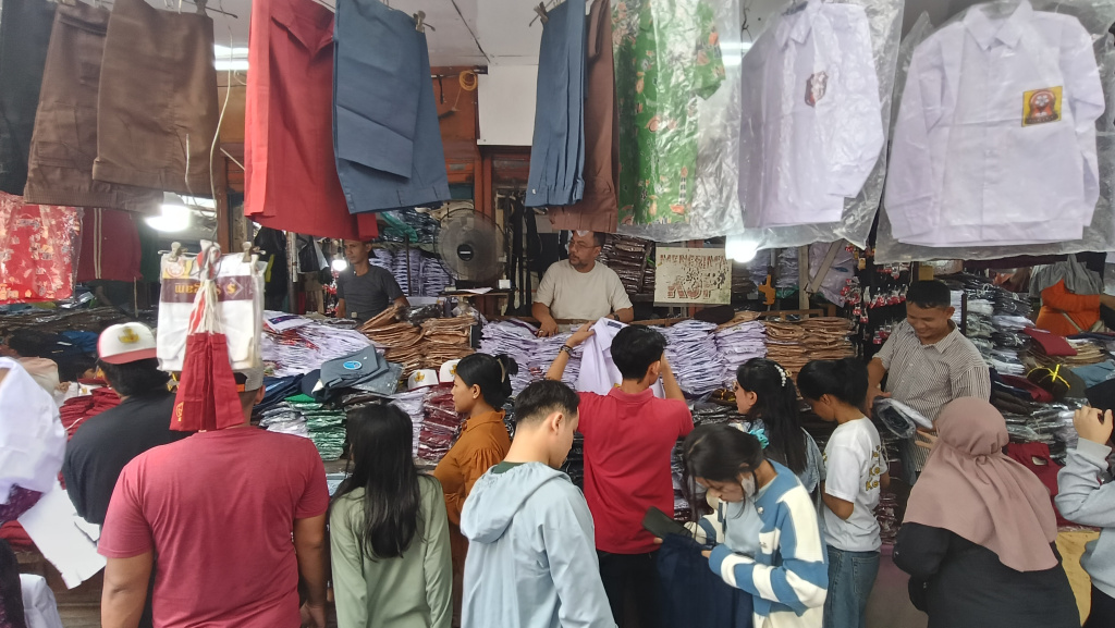 Pedagang melayani calon pembeli seragam sekolah di Pasar Jatinegara, Jakarta, Minggu (12/7/2026). (Beritanasional.com/Oke Atmaja)
