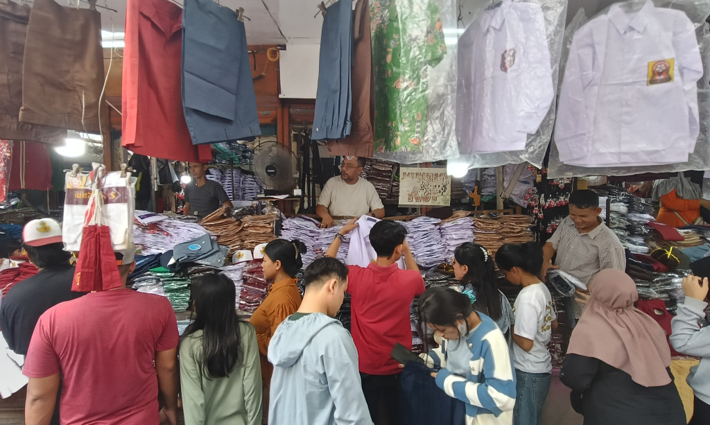 Pedagang melayani calon pembeli seragam sekolah di Pasar Jatinegara, Jakarta, Minggu (12/7/2026). (Beritanasional.com/Oke Atmaja)