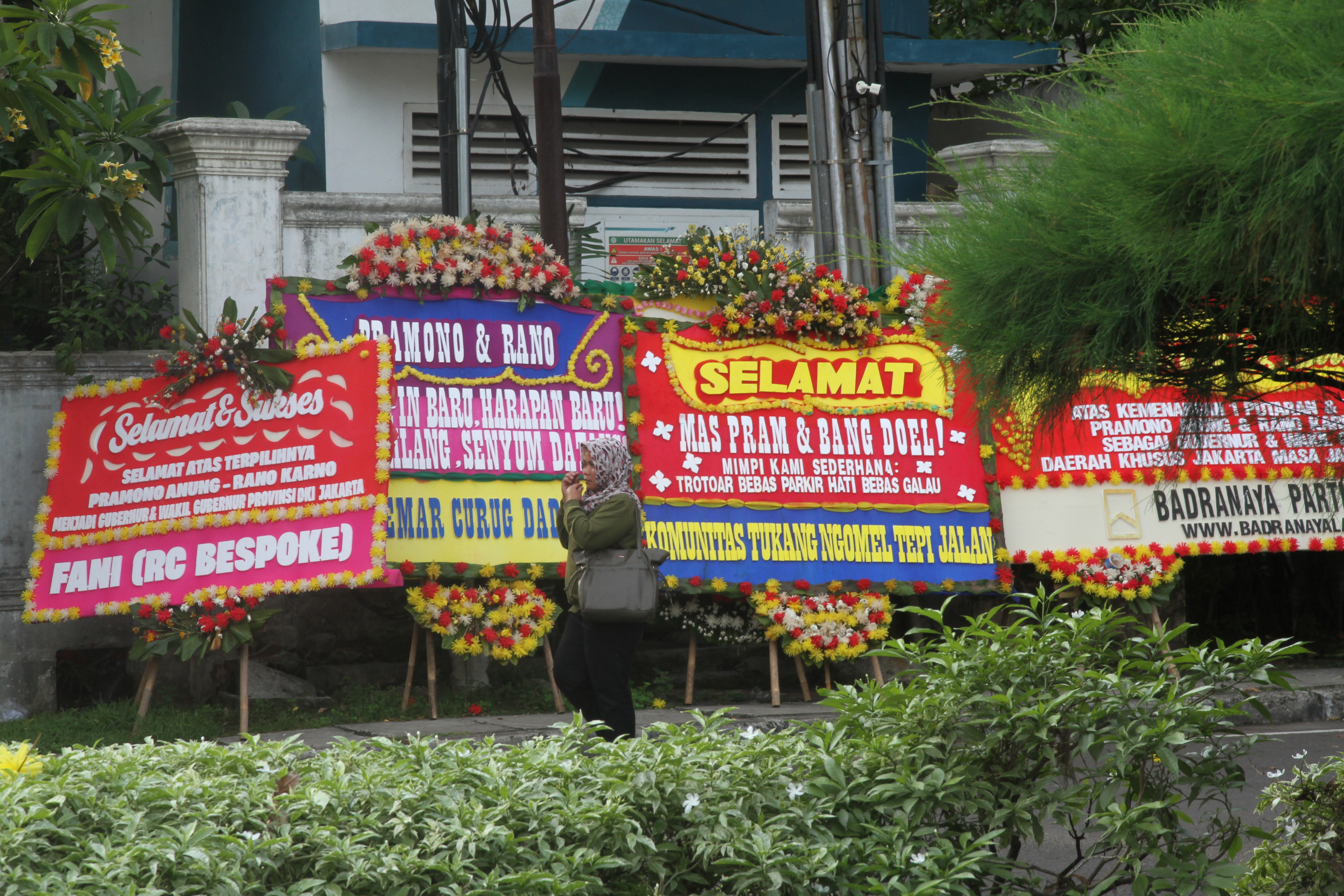 Warga melintasi karang bunga yang berjejer di sekitar Rumah Pemenangan pasangan cagub dan cawagub DKI Jakarta Pramono Anung dan Rano Karno di Jalan Cemara, Jakarta, Minggu(01/12/2024). (BeritaNasional.com/Oke Atmaja)