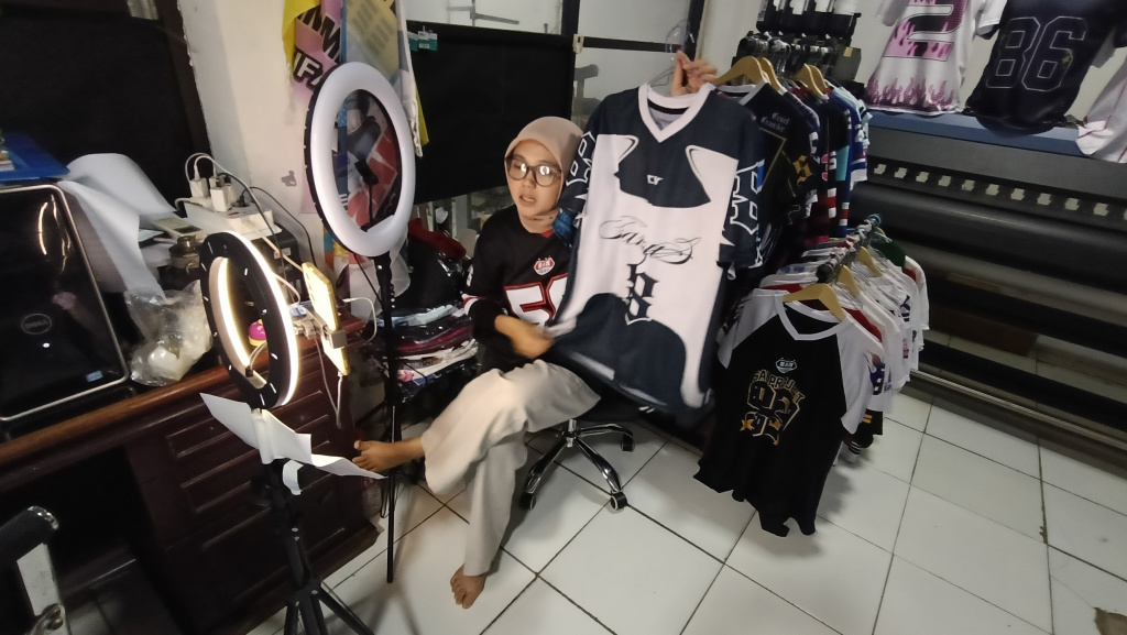 Pekerja menawarkan produk melalui siaran langsung menggunakan platform perdagangan elektronik (e-commerce) di  Industri Konveksi Rumahan Sinergi Adv Nusantara, Jagakarsa, Jakarta Selatan, Rabu (6/8/2025). (Beritanasional.com/Oke Atmaja)