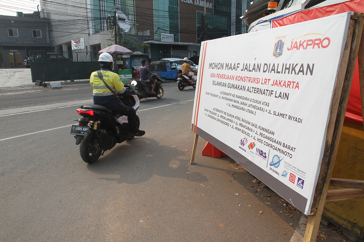 Warga melintas di depan papan informasi pengalihan arus lalu lintas akibat proyek pembangunan jalur kereta ringan atau Lintas Rel Terpadu (LRT) Jakarta Fase 1B rute Velodrome-Manggarai di Jalan Tambak, Jakarta, Minggu (15/9/2024).  (BeritaNasional.com/ Oke Atmaja)